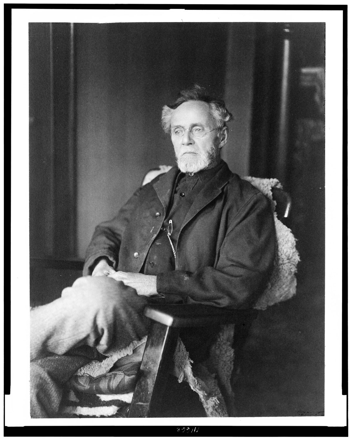 Portrait photographique d’Andrew Taylor Still, homme âgé à longue barbe blanche, assis de trois quarts, une canne à la main.